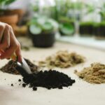 Close-up of a hand using a small shovel to sort different soil types on a table.